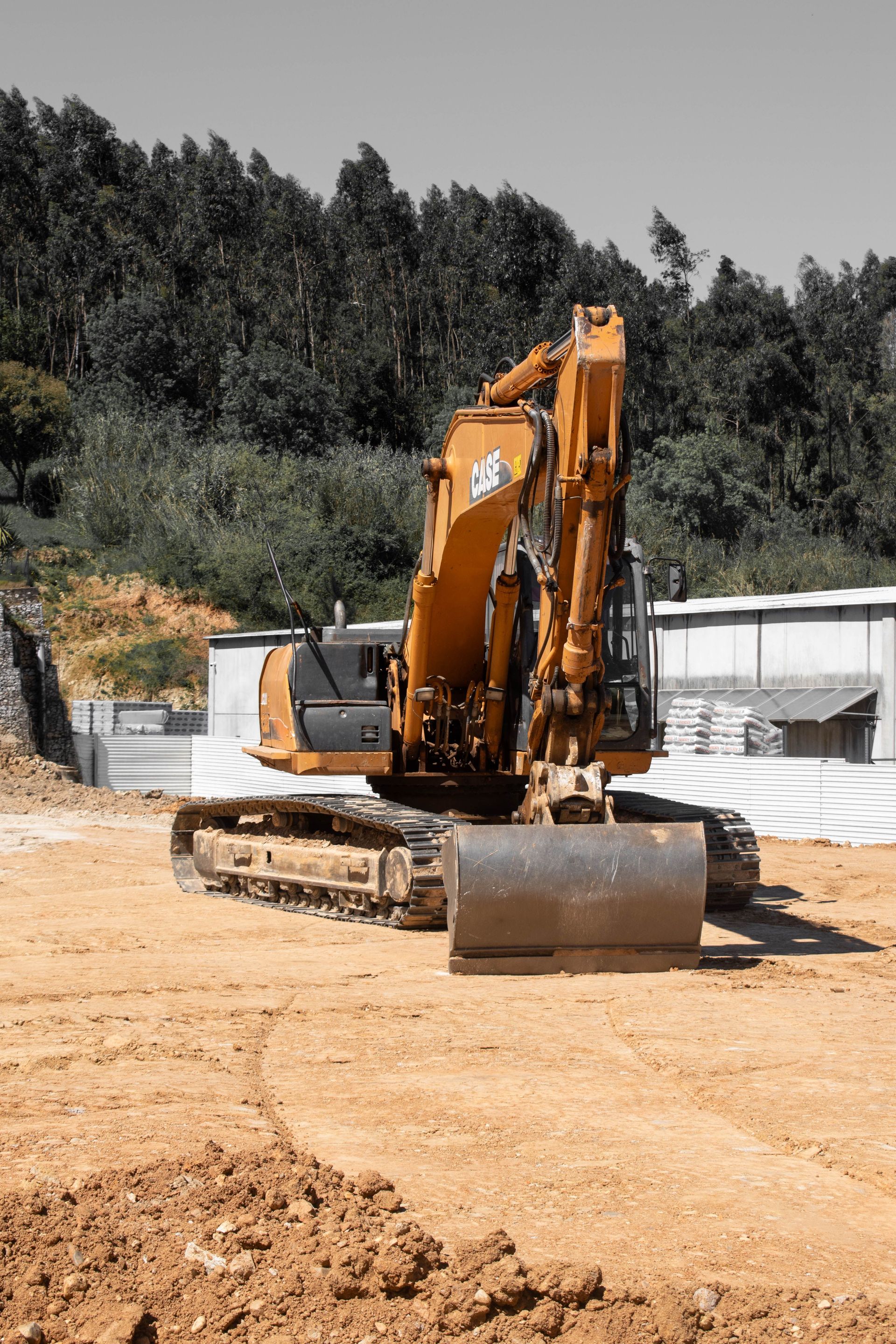 Large orange excavator on a construction site with trees in the background.