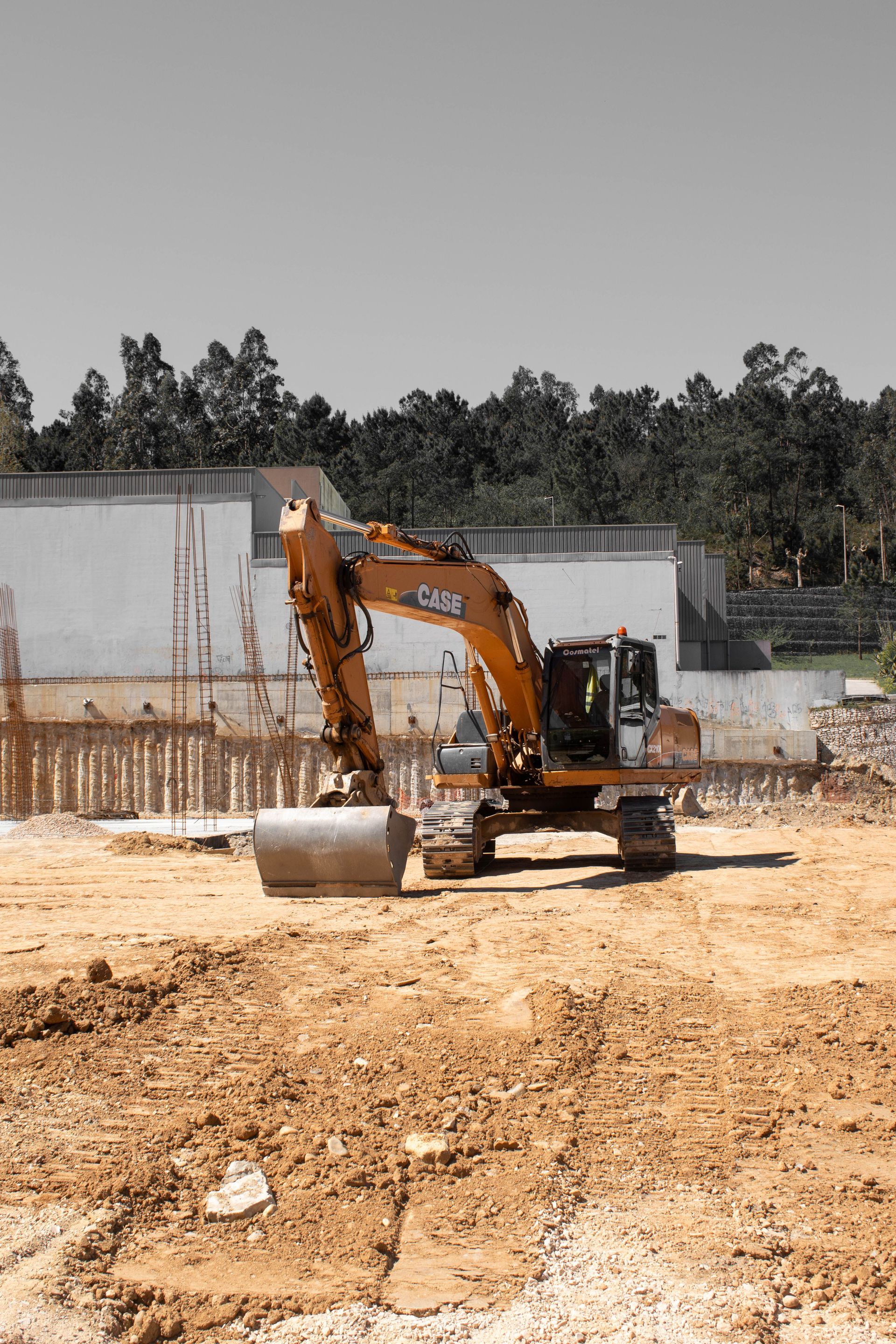 A powerful excavator operates on a construction site under a clear sky, surrounded by trees.